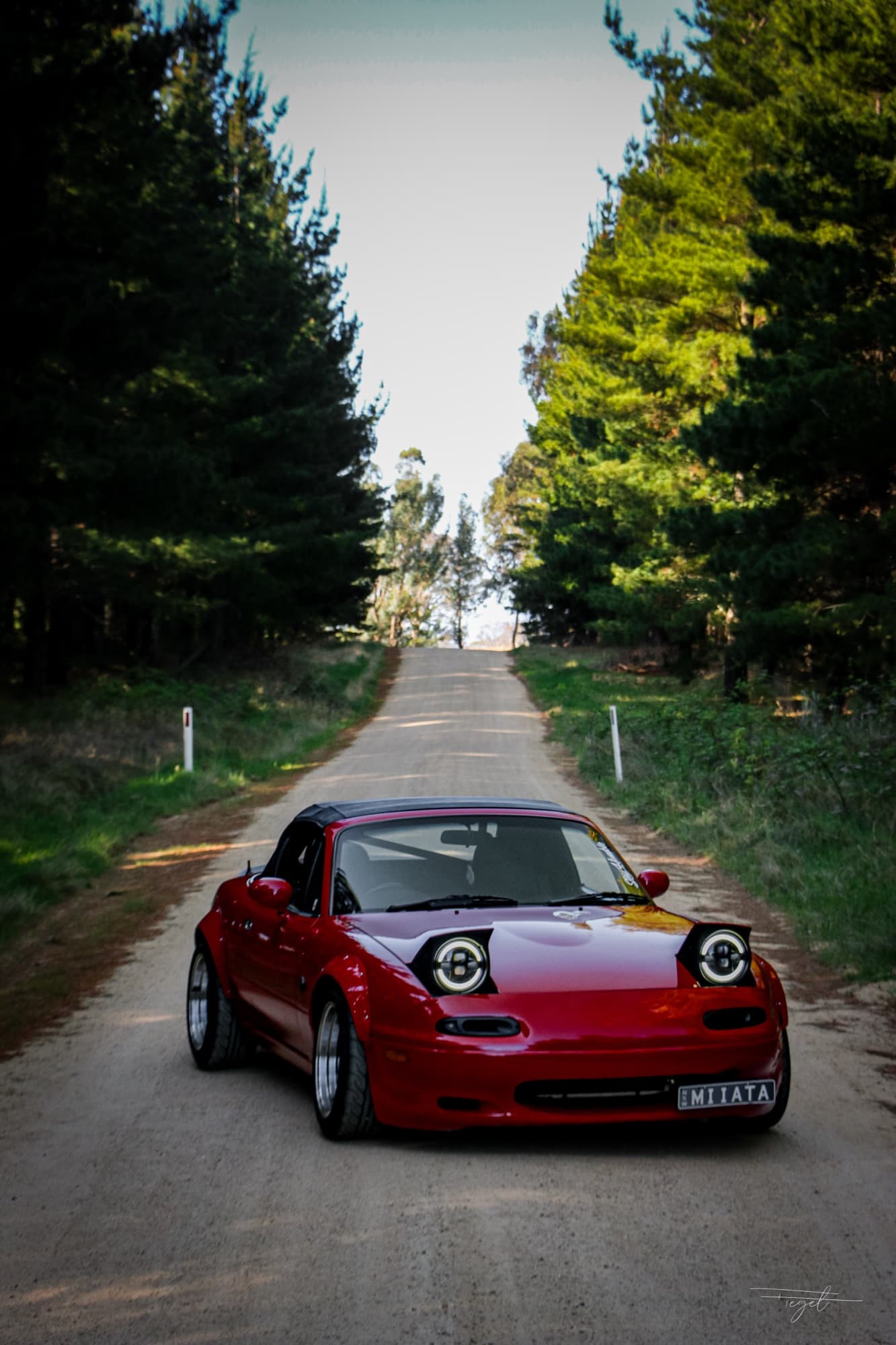 Red NA Miata on a pine-lined forest road, front-on editorial frame